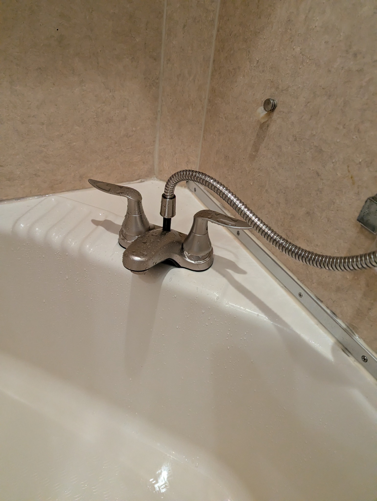 Deck-mounted two-lever faucet and connected flexible shower hose beside the tub